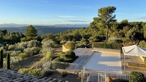 Terraza en la azotea con vistas a un paisaje montañoso, rodeada de árboles frondosos y cielo despejado.