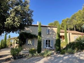 A house with a gravel driveway, a patio with outdoor furniture, and a garden with various plants and trees.