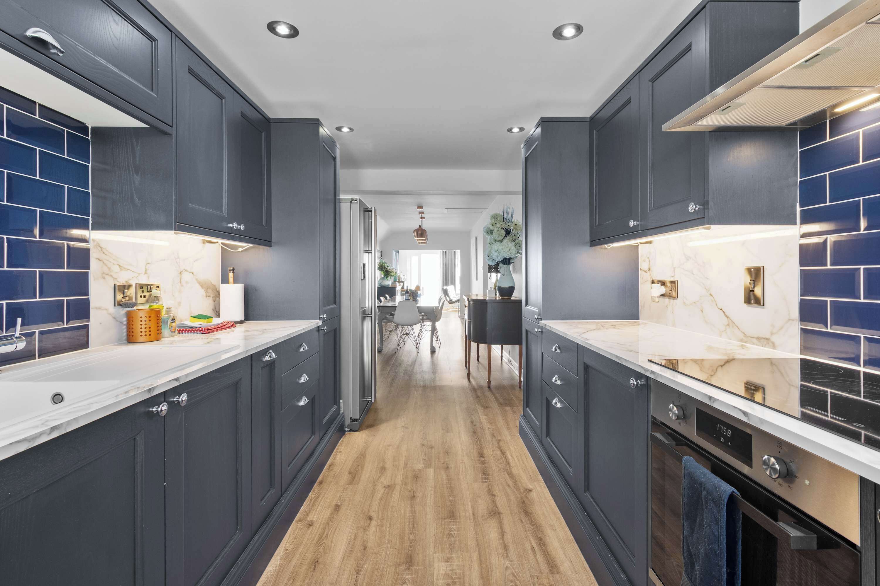 Une cuisine moderne avec des meubles de couleur sombre, des plans de travail en marbre et un plancher en bois.