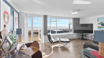 Un salon moderne doté d’un grand téléviseur, de sièges confortables et d’un balcon offrant une vue sur la mer.