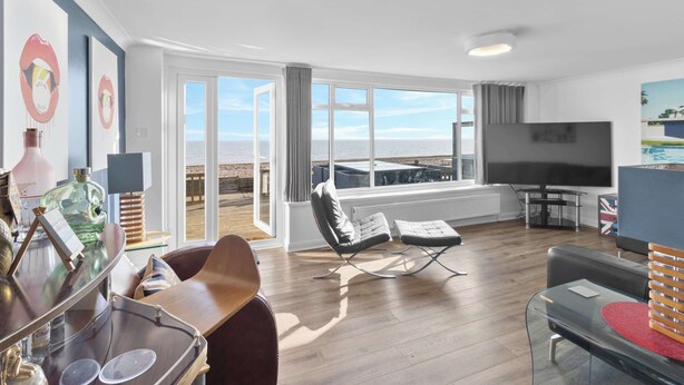 Una sala de estar moderna con un televisor grande, asientos cómodos y un balcón con vistas al mar.