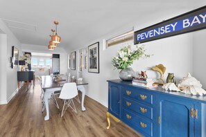 A modern interior with a dining area, a blue cabinet with decorative items, and a 'PEVENSEY BAY' sign on the wall.