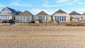 Una hilera de casas de playa con ventanas amplias, una terraza de madera y una playa de guijarros al frente.