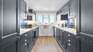 Una cocina estrecha con muebles oscuros, encimeras blancas y suelo de madera.