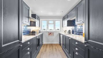 Une cuisine étroite avec des meubles de couleur sombre, des plans de travail blancs et un plancher en bois.