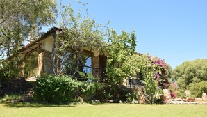 A rustic house with a stone facade, a balcony, and lush greenery.