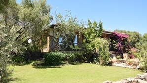 A stone building with a tiled roof, surrounded by a well-maintained garden with various plants and a clear blue sky.