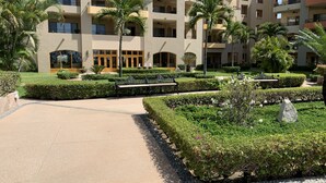 Un hôtel à plusieurs étages doté de balcons, d’une cour centrale avec des bancs et de palmiers.