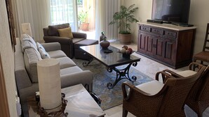 Un salon comprenant un canapé, des fauteuils, une table basse, un téléviseur et un meuble.