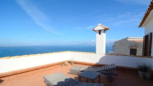 A terrace with outdoor furniture, a stone wall, and a view of the sea.