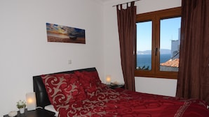 A bedroom with a bed, a nightstand, a lamp, a painting, and a window with curtains.