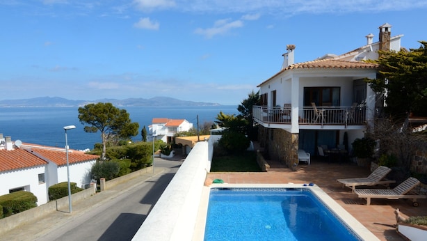 A poolside view of a two-story house with a clear view of the sea.