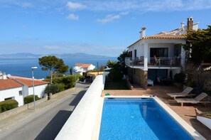 Blick auf einen Pool und ein zweistöckiges Haus, mit freiem Blick auf das Meer.