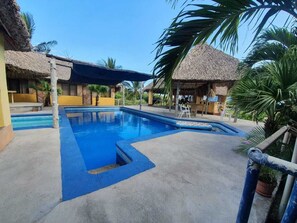 A swimming pool with a blue edge, surrounded by thatched-roof structures and palm trees.