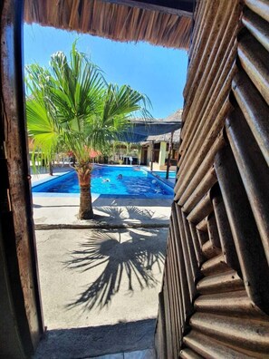 A pool area with a palm tree, a thatched roof structure, and a concrete pathway.