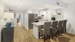 Una cocina moderna con armarios blancos, una isla central y un comedor con sillas de mimbre.
