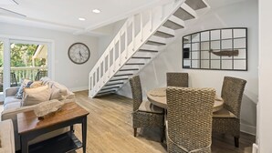 Una sala moderna con una escalera, un comedor con sillas de mimbre, una mesa redonda y un reloj grande en la pared.