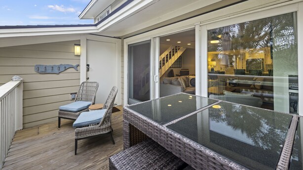 Un patio techado al aire libre con mobiliario de mimbre, una mesa de vidrio y vistas hacia la casa.