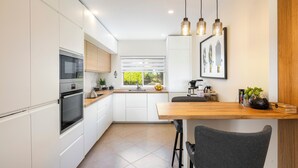 Cozinha moderna com armários brancos, forno embutido, bancada de madeira e área de refeições com uma cadeira.