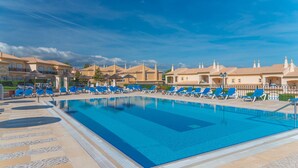 Uma piscina grande com cadeiras de descanso azuis e um deck revestido de azulejos.