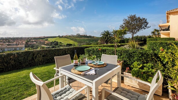 Uma área de refeições ao ar livre com uma mesa posta para dois, cercada por vegetação exuberante e uma vista panorâmica de uma paisagem montanhosa.