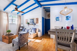 Ein geräumiges Wohnzimmer mit Holzboden, einer Couch, einem Esstisch und einem Deckenventilator.