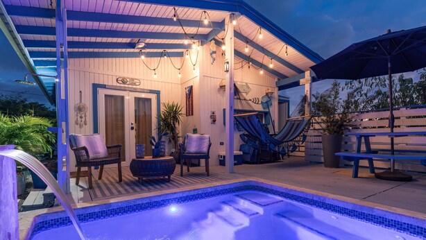 Ett poolområde med ett bubbelbad, solstolar och en täckt uteplats med ljusslingor.