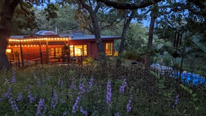 Een rustieke chalet met een glazen uitbouw, omgeven door wilde bloemen en bomen.