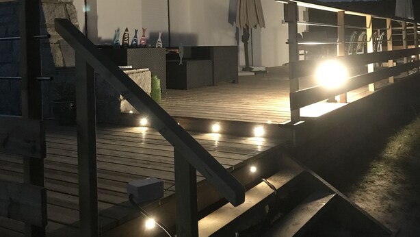 A wooden deck with steps leading to a covered area with outdoor seating.