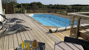A wooden deck with a pool, lounge chairs, and a table with drinks.