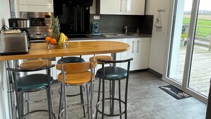 A modern kitchen with a central island, bar stools, and a view through the glass door.