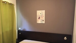 A room with a bed, a headboard, a wall-mounted artwork, and a green curtain. - Corsica: apartment in residence *** 6 people - swimming pool at 100m beach (Linguizzetta)