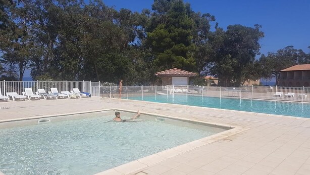 A swimming pool with a tiled deck, lounge chairs, and a small building in the background. - Corsica: apartment in residence *** 6 people - swimming pool at 100m beach (Linguizzetta)