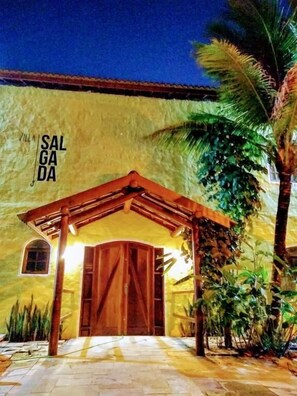 A villa with a covered entrance, a stone pathway, and a palm tree. - Villa Salgada Maresias (São Sebastião)