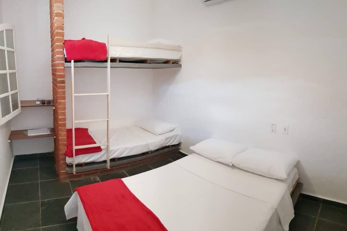 Ein Schlafsaalzimmer mit zwei Betten, einem Etagenbett, einer Leiter, einem Fenster und einer Wand-Klimaanlage.