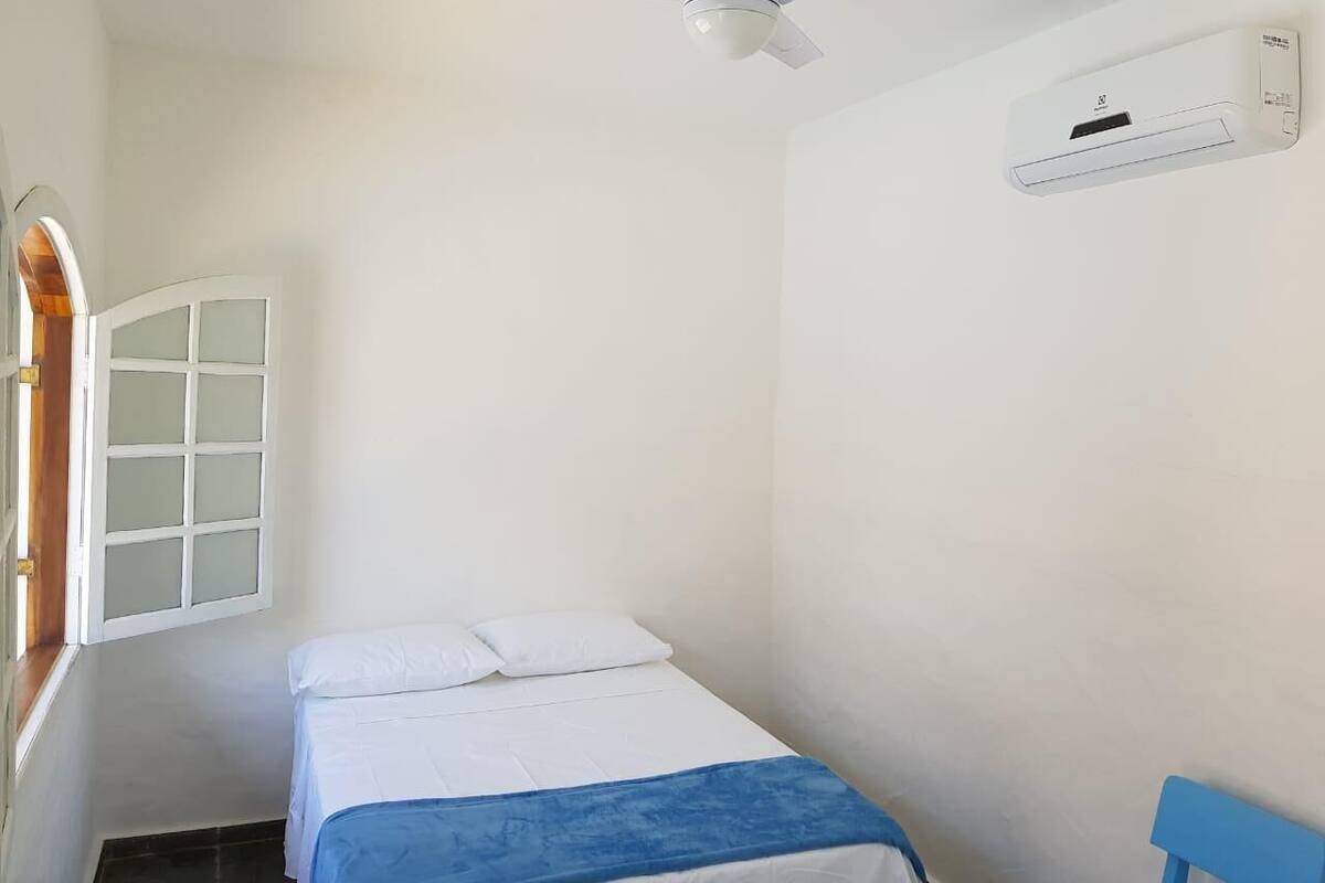 Ein kleines, sauberes Zimmer mit einem Einzelbett, einem Deckenventilator und einer Wand-Klimaanlage.