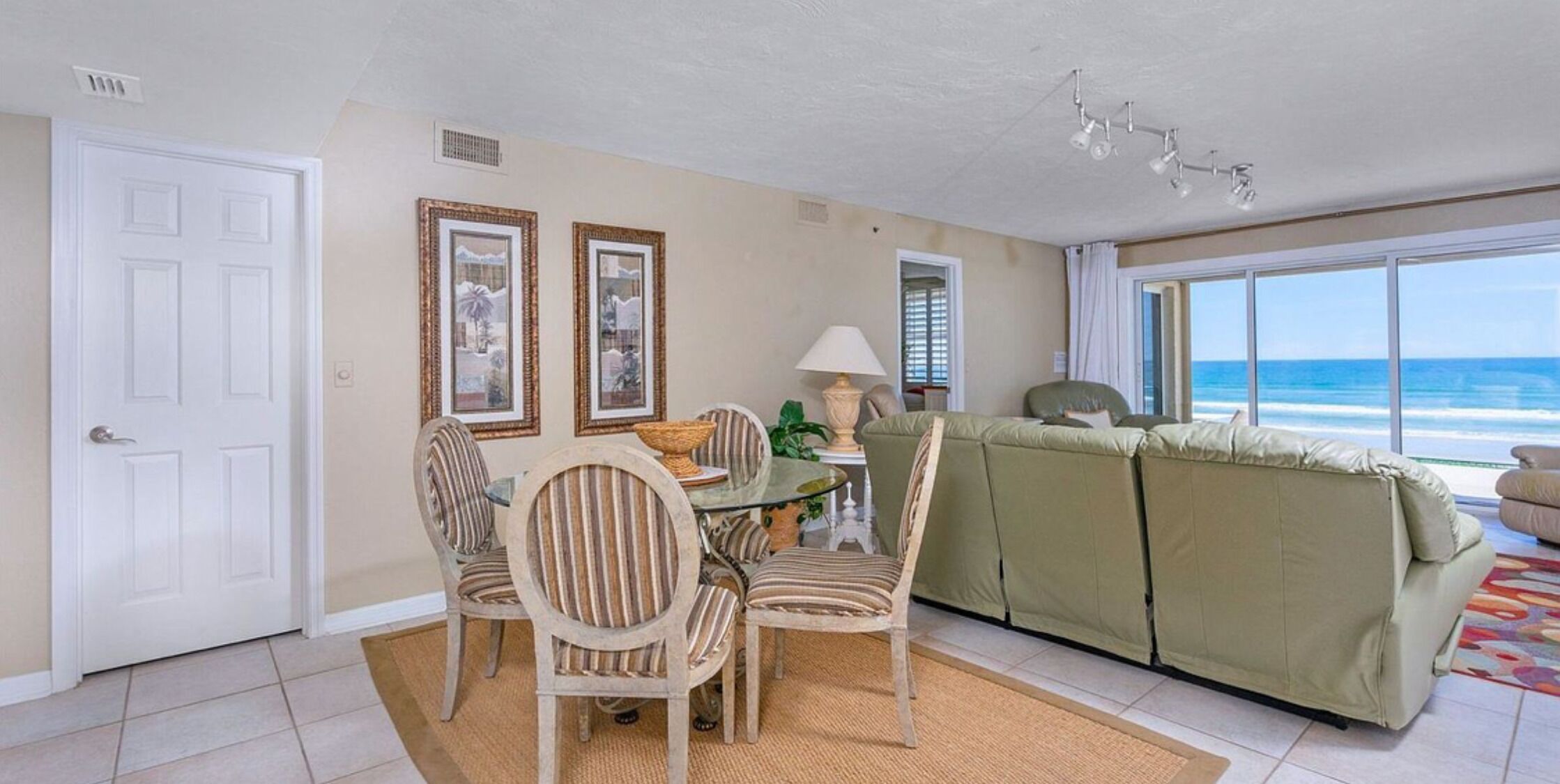 A living room with a dining area, a green sofa, and a view of the ocean.