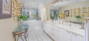 Une salle de bain moderne avec une table en verre, des meubles blancs et des œuvres d’art décoratives au mur.