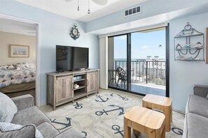 A modern living room with a large TV, wooden furniture, and a view of the city through a balcony. - Fantastic Ocean View and Outdoor Pool, 1 Bedroom! (Ocean City)