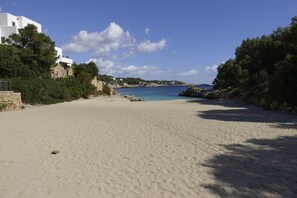 A sandy beach with white buildings and rocky outcrops.