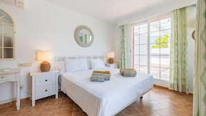 A hotel room with a large bed, two bedside tables with lamps, a round mirror, and a view through a sliding glass door. - Beautiful beachfront private villa with swimming pool in Cala d'Or (Cala d'Or)