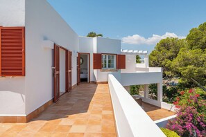 A modern building with a white exterior, red shutters, and a tiled terrace.