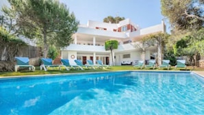 A swimming pool with lounge chairs and a building with multiple floors and balconies. - Beautiful beachfront private villa with swimming pool in Cala d'Or (Cala d'Or)