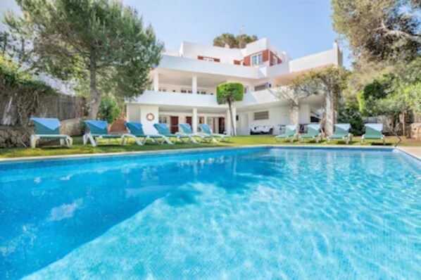 A swimming pool with lounge chairs and a building with multiple floors and balconies.