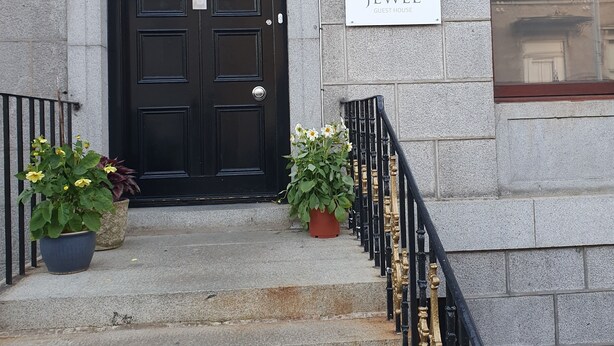 A building entrance with a black door marked "148", a sign reading "JEWEL GUEST HOUSE", and a staircase with a black and gold railing. - Jewel Guest House (Aberdeen)