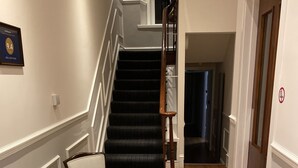 A hallway with a wooden floor, a chair, a glass table with a map, and a staircase with dark steps. - Jewel Guest House (Aberdeen)
