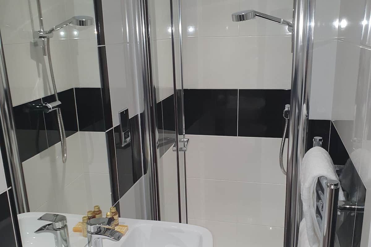 A modern bathroom with a glass-enclosed shower, a white sink with chrome fixtures, and black and white tiled walls.