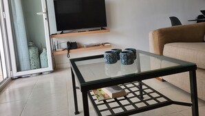 Un salon moderne avec une table basse en verre, un canapé, un téléviseur à écran plat et des vases décoratifs.
