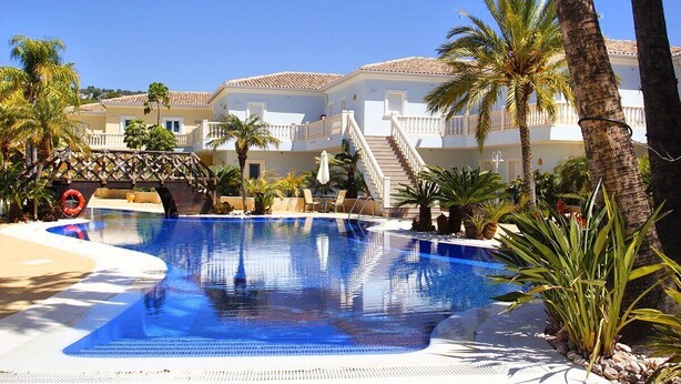 Une piscine entourée de palmiers et un bâtiment doté d’un toit en tuiles.