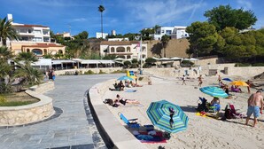 Une plage avec un sentier de pierres en forme de courbe menant au bord de l’eau, des parasols et des gens qui se détendent.